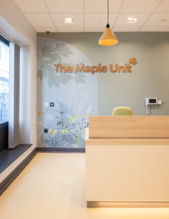 Subtle blue and green biophilic artwork below wooden lettering 'The Maple Unit' at the welcoming entrance