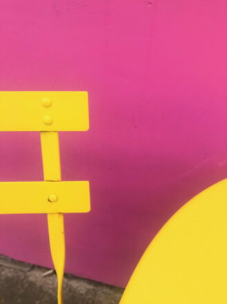 A photograph of a bright yellow table and chair against a bright pink wall