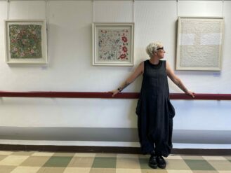 Artist, Gina May Selene in front of a gallery of her hand embroidered artwork