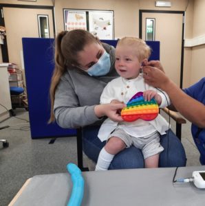 A baby sitting on their mother's lap while having a hearing test done