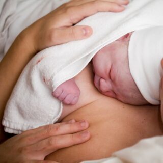 A parent embracing their newborn child on their chest with a towel covering them.