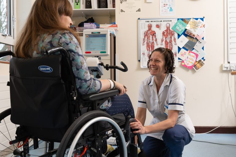 NHS healthcare professional talking to a patient in a wheelchair.