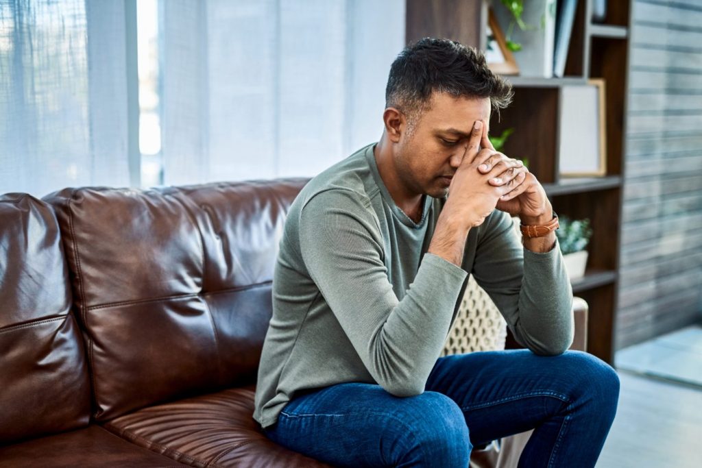 a man sitting on a sofa holding his head in his hands