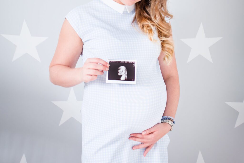 a pregnant lady in a white dress holding her belly and clutching a scan photo