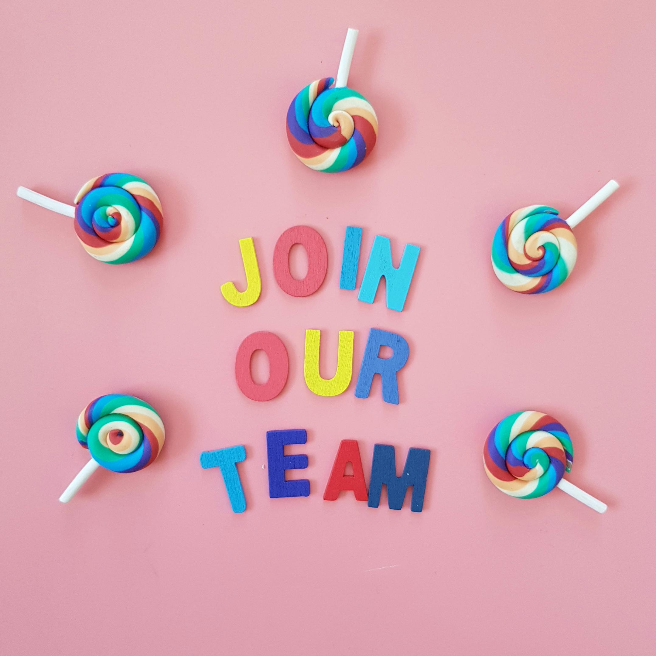 join our team written in bright colour letters on a pink background with four multicoloured lollipops