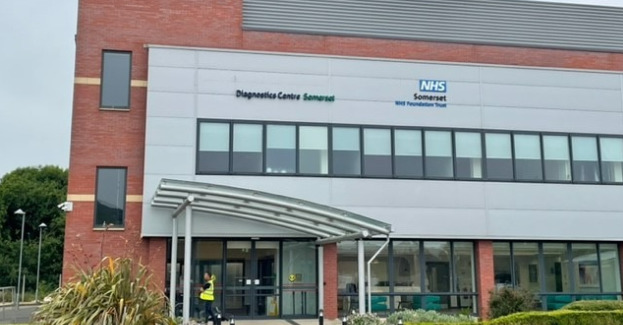 Image of the Taunton Diagnostic Centre. The image shows a large red brick building with grey panelling at the front of the building. The NHS logo and the name 
