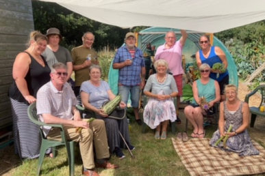 image of several people sat on camping chairs holding fruits vegatables and flowers they have grown