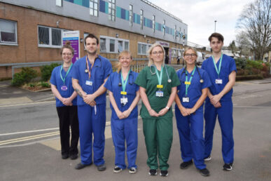 Six colleagues from Yeovil Hospital stood in front of the main Yeovil Hospital entrance. Five colleagues are wearing blue scrubs with Lanyards, and one colleague wearing green scrubs. They are all Physician Associates.