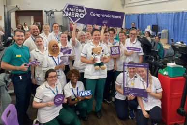 A photo of occupational therapist Emily Alden holding a teddy bear with her many colleagues in the background.