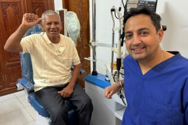 A photo of Somerset ophthalmology consultant Mr Indy Sian sat with a patient in a treatment room in rural Cambodia.