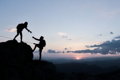 A photo of a silhouette person helping a person climb up a hill.
