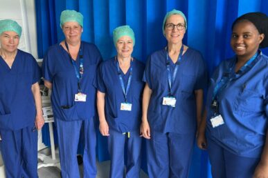 Colleagues who work at Minehead Hospital's operating theatres are stood next to a blue operating theatre curtain.
