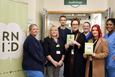 A photo of colleagues who work for the audiology service at Musgrove Park Hospital, stood in a hospital corridor with colleagues from the Royal National Institute for Deaf People. They are holding up leaflets.