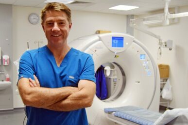 A photo of radiologist Cenydd Thomas standing next to a scanning machine at Yeovil Hospital.