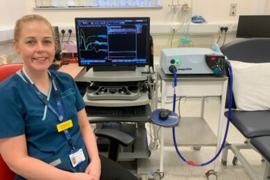 A photo of Diane Boothman sat next to a transcranial magnetic stimulation machine in a treatment room.