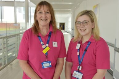 A photo of two learning disabilities nurses in their pink uniforms stood in a corridor.