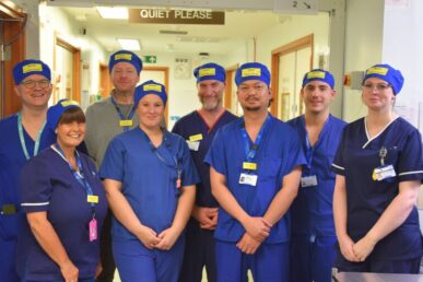 A group of colleagues who work at the orthopaedic operating theatres at Musgrove Park Hospital wearing scrubs and reusable hats. They are standing up.