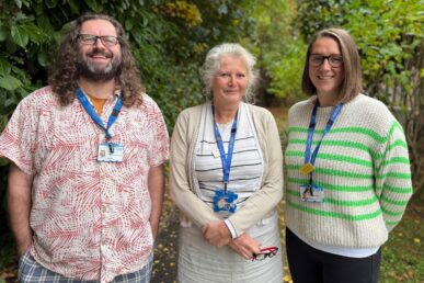 A photo of consultant psychotherapist Adrian Hayes, research nurse team leader Carinna Vickers and clinical trials officer Alicia Long stood in front of trees.