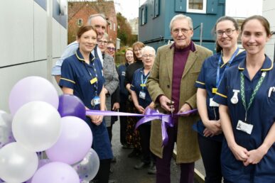 People gathered at the ramp up to the new stoma care department building at Yeovil Hospital for the official opening. Two nurses and a patient are stood close to a ribbon, which is ready for cutting.