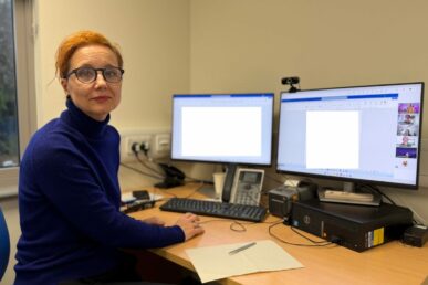 A photo of Ivona Ramoiu - lead dermatology clinical practitioner - sat at a desk with a computer in a clinic room at Yeovil Hospital.