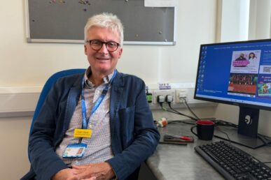 A photo of Doctor Robert Stone - a respiratory consultant - sat on a chair next to a computer screen.