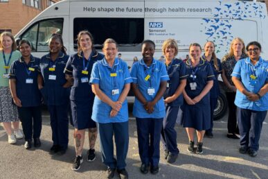 A group of NHS research colleagues in uniform stood outside a mobile research unit.